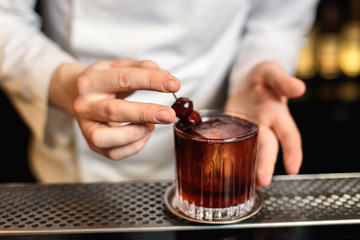 Bartender putting a garnish cherry on a rocks glass with a drink. Lifestyle horizontal image.