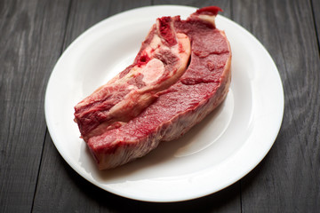 Raw veal steak on a white plate on a black wooden background.