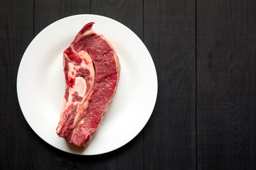Raw veal steak on a white plate on a black wooden background.
