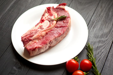 Raw veal steak on a white plate on a black wooden background.