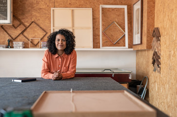 Fototapeta na wymiar Smiling woman working at a table in her framing workshop