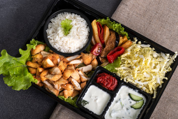 Traditional doner kebab in a black plastic container, sour cream, white boiled rice, roast meat,...