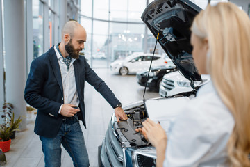 Man and saleslady choosing auto in car dealership
