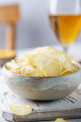 Crunchy delicious potato chips in a bowl with beer for a tasty snack break on light background