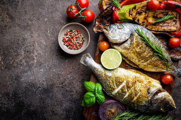 Baked Dorado fish, sea bream with grilled vegetables, herbs and seasonings, top view
