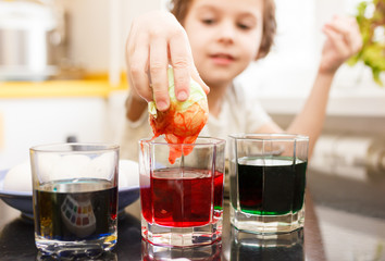 boy dips an egg in a glass with paint. Boy paints easter eggs