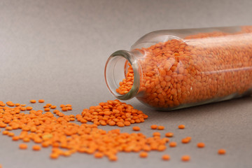 red split lentils scattered on a grey background from glass jar