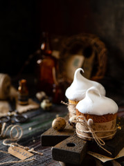two baked orthodox easter cakes with white meringue glaze on top stands on wooden boards on rustic table with qual eggs, willow