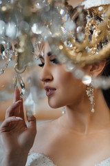 The charming bride is standing near the chandelier. Female Elegant wedding make up for the wedding