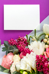 Flowers mock up gift card. Congratulations card in bouquet of roses, tulips, eucalyptus on purple background. White blank card with space for text, frame mockup for invitation. Spring festive flowers.