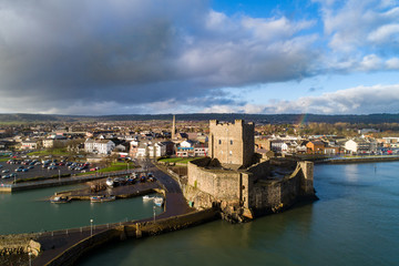 Fototapeta na wymiar Medieval Norman Castle, harbor with boat ramp and wave breaker in Carrickfergus near Belfast, Northern Ireland, UK. Aerial view in sunset light in winter. Town and stormy clouds in the background