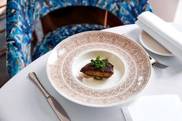 Foie gras scallops decorated with greens in sauce on plate with patterns