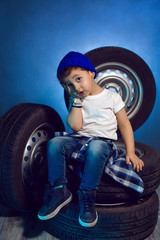 boy in a white t shirt shirt and hat sits on a background of car wheels