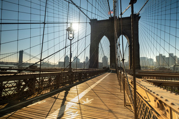 Early morning sun rises on the path of the Brooklyn Bridge over the East River connecting Manhattan New York to Brooklyn USA