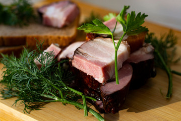 smoked brisket on a wooden board with bread, dill and parsley.