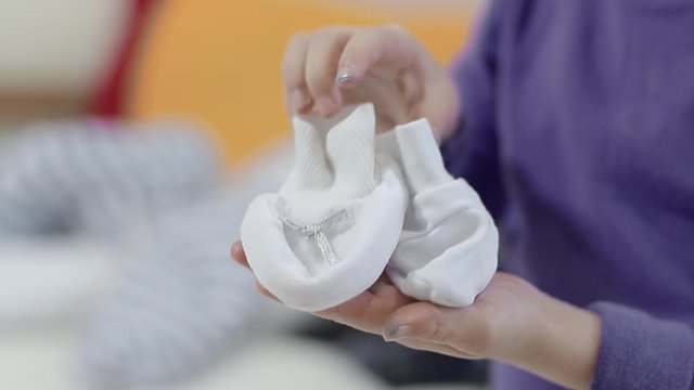 Children's hands hold small white shoes for the baby on the day of Baptism.