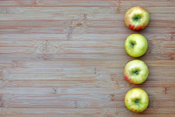 A row of four fresh organic apples lined up on the right side of a bamboo board