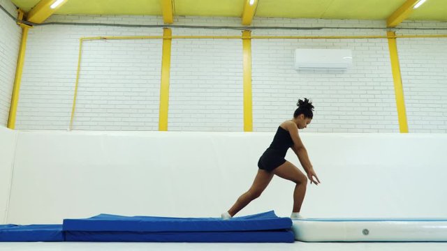 Black girl practicing back flips on mats in gym