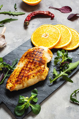 Grilled chicken fillets with orange on slate plate. Gray concrete background