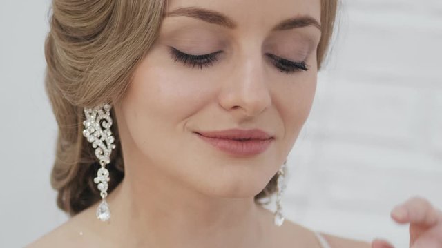 Big close up shot of young blonde bride with wedding hairstyle in tiara earrings wedding gown posing in trendy wedding salon showing gorgeous wedding makeup teasing and seductively looking in camera