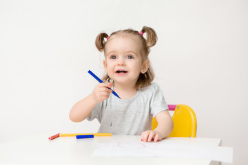 child a girl two years old sits at a table and draws on a white background