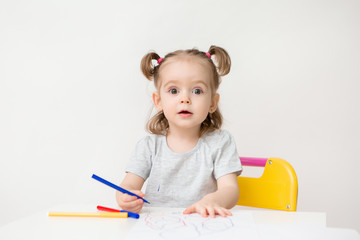 child a girl two years old sits at a table and draws on a white background