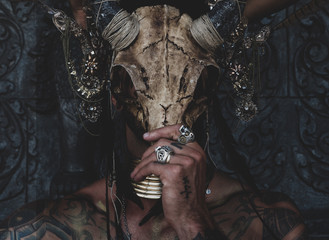 Tattooed masked skull ethnic pagan shaman sit on stage an ancient temple.