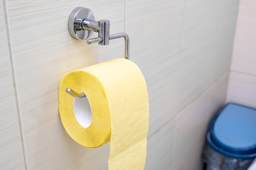 A roll of yellow toilet paper hanging on a wall fixture in a rest room, digestive problems concept