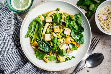 Vegan thai green curry with tofu, sweet potato, corn and spinach, top view.