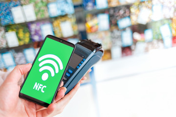 Women's hands are held by a payment terminal and a man pays for a purchase using a smartphone.On the phone screen, the wi-fi network. Copy space. The concept of NFC, business and banking transactions