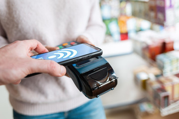 The seller holds a payment terminal, and the man pays for the purchase using a smartphone, online. On the phone screen-wi-fi network. NFC concept, business and banking operations