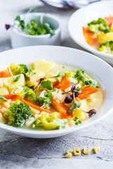 Healthy kids alphabet soup with broccoli, carrot and potato in white plates.