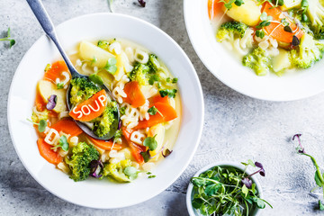 Healthy kids alphabet soup with broccoli, carrot and potato in white plates, top view.
