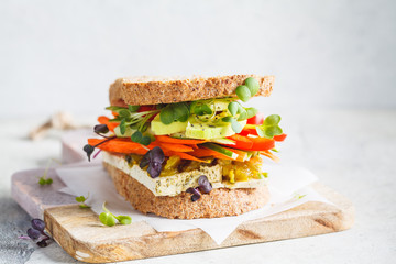 Vegan sandwich with tofu, pepper, carrot, hummus and green dressing on the board.