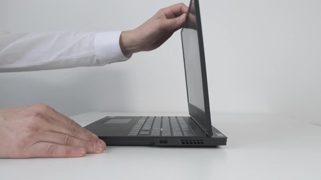 Male hand opens laptop on white nable. Close up.