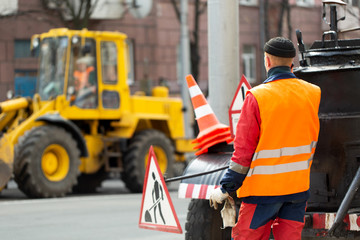 An employee in an orange uniform controls the process of road repairs.