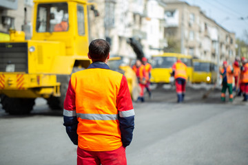 An employee in an orange uniform controls the process of road repairs.