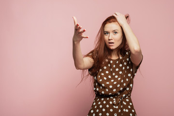 The red-haired girl is surprised and shocked. Woman experiences an emotion of rage on a pink background in the studio