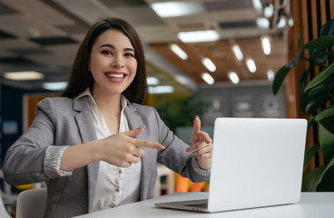 Happy emotional woman showing fingers on laptop computer, looking at camera and smiling. Online shopping, cash back, discount sales, hot deal concept