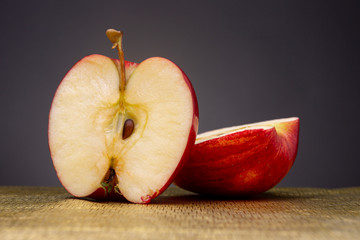 Vibrant bright red apple cut in half with one part laying down and the other standing up in front with seed on a partly out of focus golden surface contrasted against a dark grey studio background