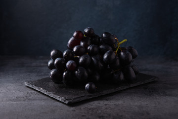 a cluster of juicy black grapes lies on a black slate on a dark gray table
