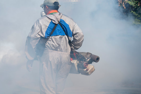 Softly Focus Of Healthcare Worker Using Fogging Machine Spraying Chemical To Eliminate Mosquitoes And Prevent Dengue Fever In The Midst Of Many Chemical Fumes At General Location In Community