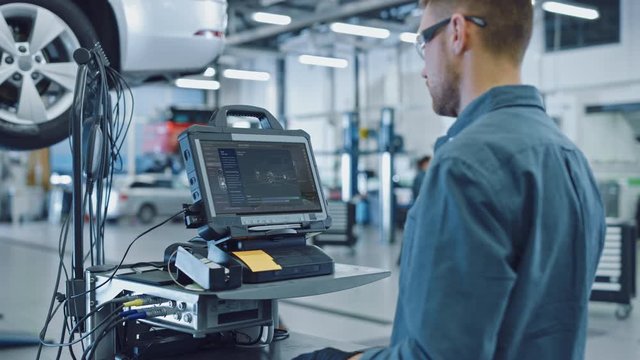 Car Service Manager or Mechanic is Running an Interactive Diagnostics Software on an Advanced Computer. Specialist Inspecting the Vehicle in Order to Find Broken Components and Errors in Data Logs.