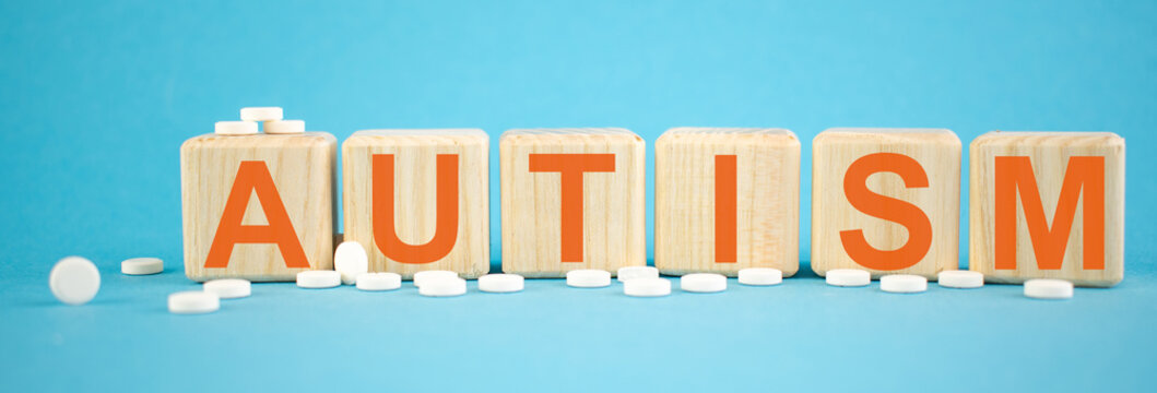 Autism - word made on wooden cubes on light blue backround with tablets (pills) around. Healthy care and medical concept.