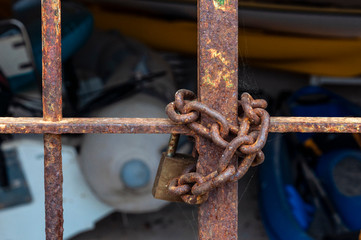 Rusty padlock closing a rusty metal gate. At the bottom out of focus, recreational boats