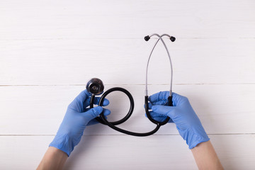 Top view aerial image of healthcare accessories & medical concept. Hands in blue medical gloves hold a stethoscope.