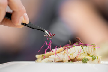 Chef with tweezers decorates with microgreens sprouts fish dish. Concept high art cooking, food...