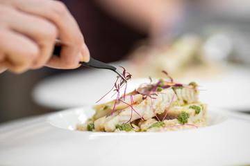 Chef with tweezers decorates with microgreens sprouts fish dish. Concept high art cooking, food...