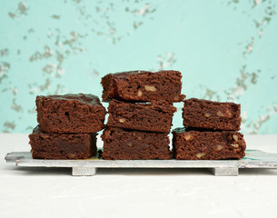 stack of square baked pieces of brownie chocolate cake with walnuts on a wooden board