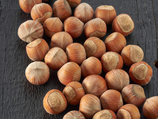 Hazelnuts lie in a plate on a black wooden background